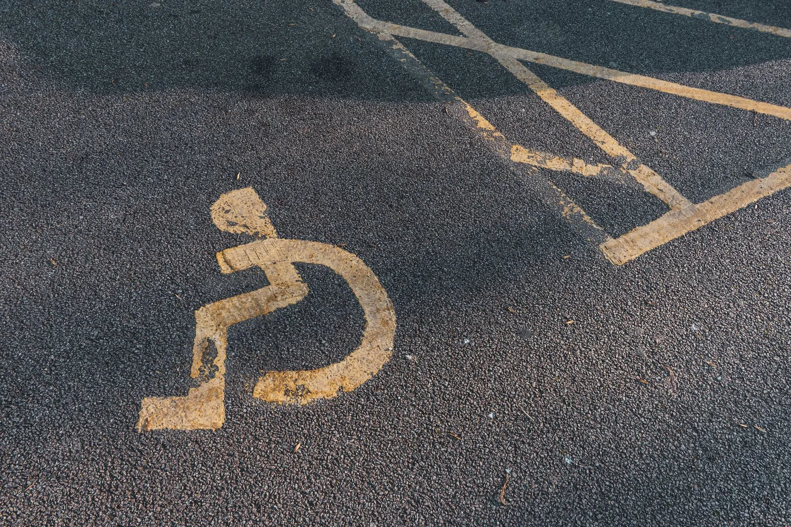 A faded accessibility symbol painted on asphalt pavement