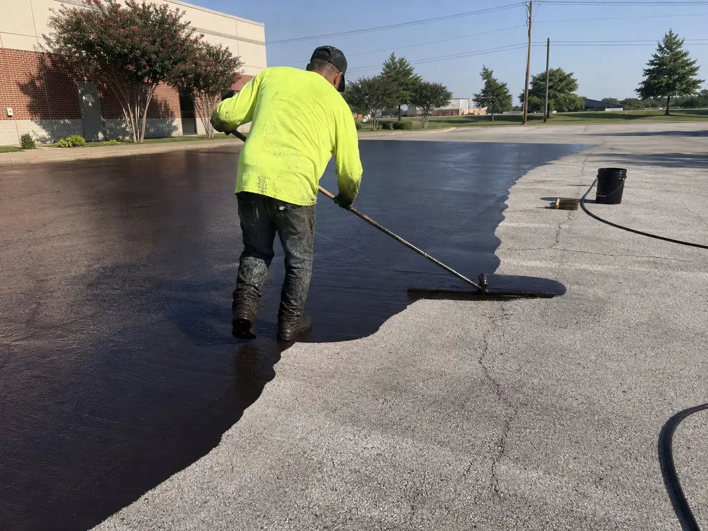 Fresh sealer being squeegeed across a commercial asphalt parking lot